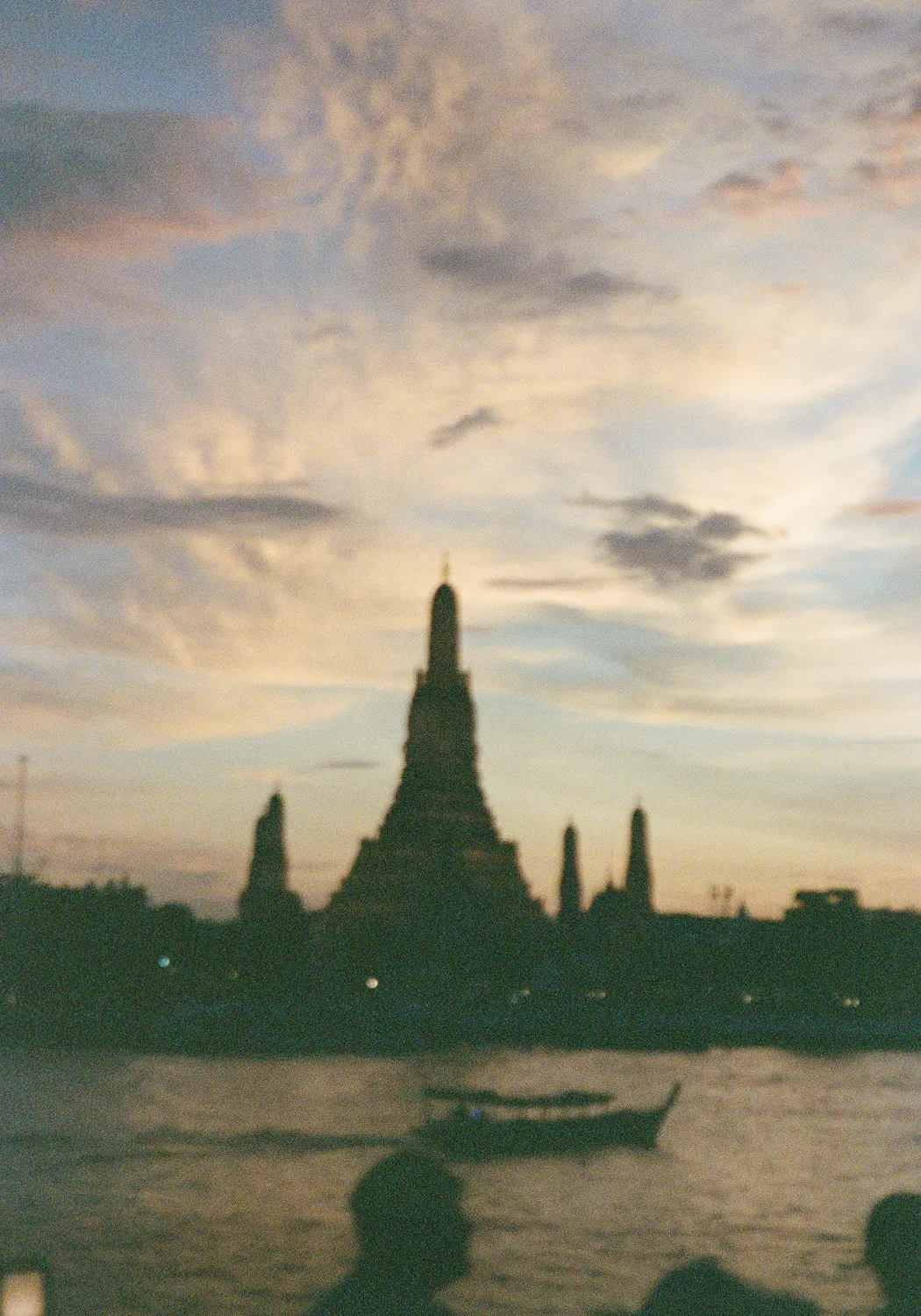 Silhouetted temple spires and a boat on a river at sunset with a colorful cloudy sky.