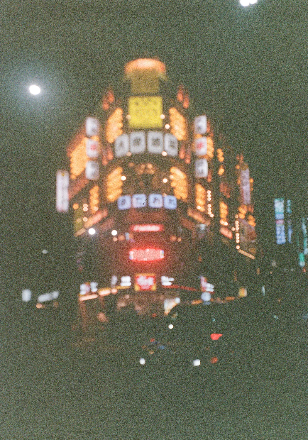Nighttime city street scene with illuminated building signs and car headlights in the foreground.