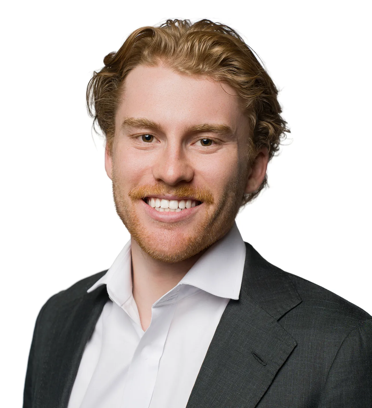 Smiling young man with red hair and beard wearing a white shirt and dark blazer on a white background.
