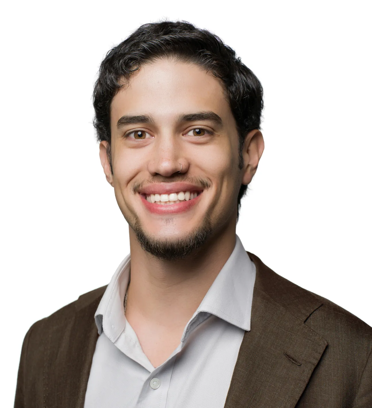 Smiling young man with short curly hair, a goatee, nose ring, white shirt, and brown blazer on white background.